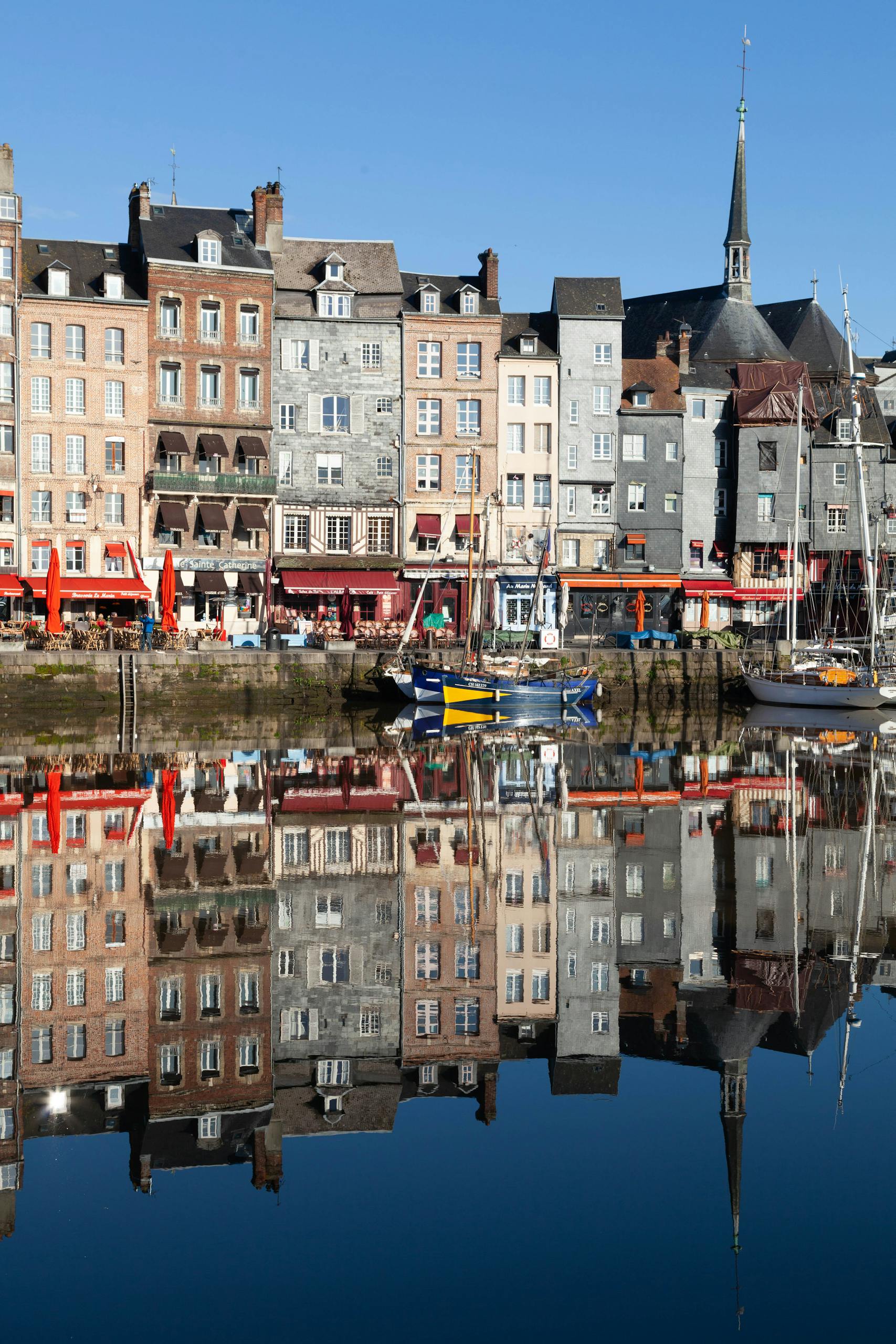Scenic view of Honfleur's old town reflecting in calm harbour waters on a clear day.